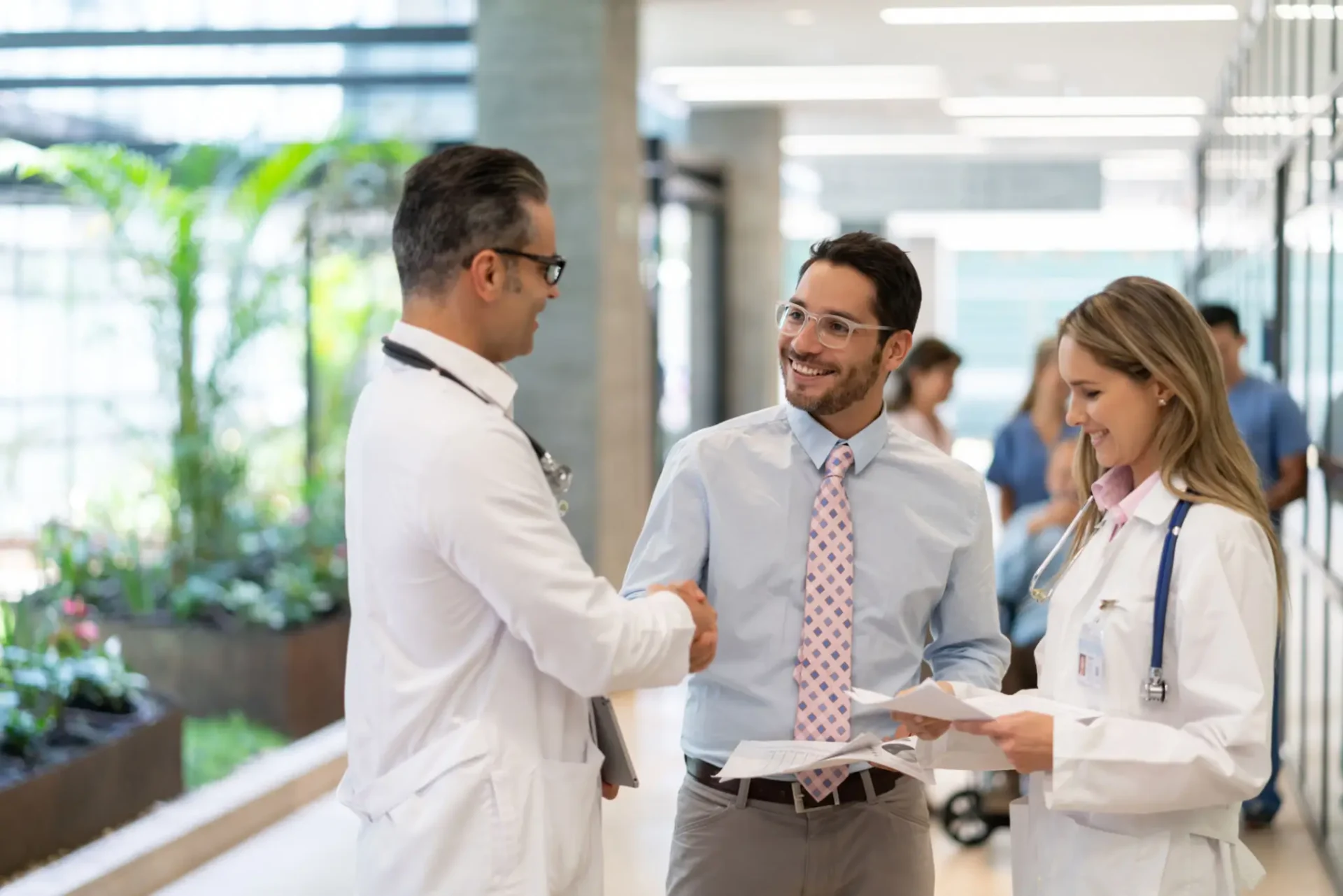 Doctor and businessman shaking hands in a hospital lobby.